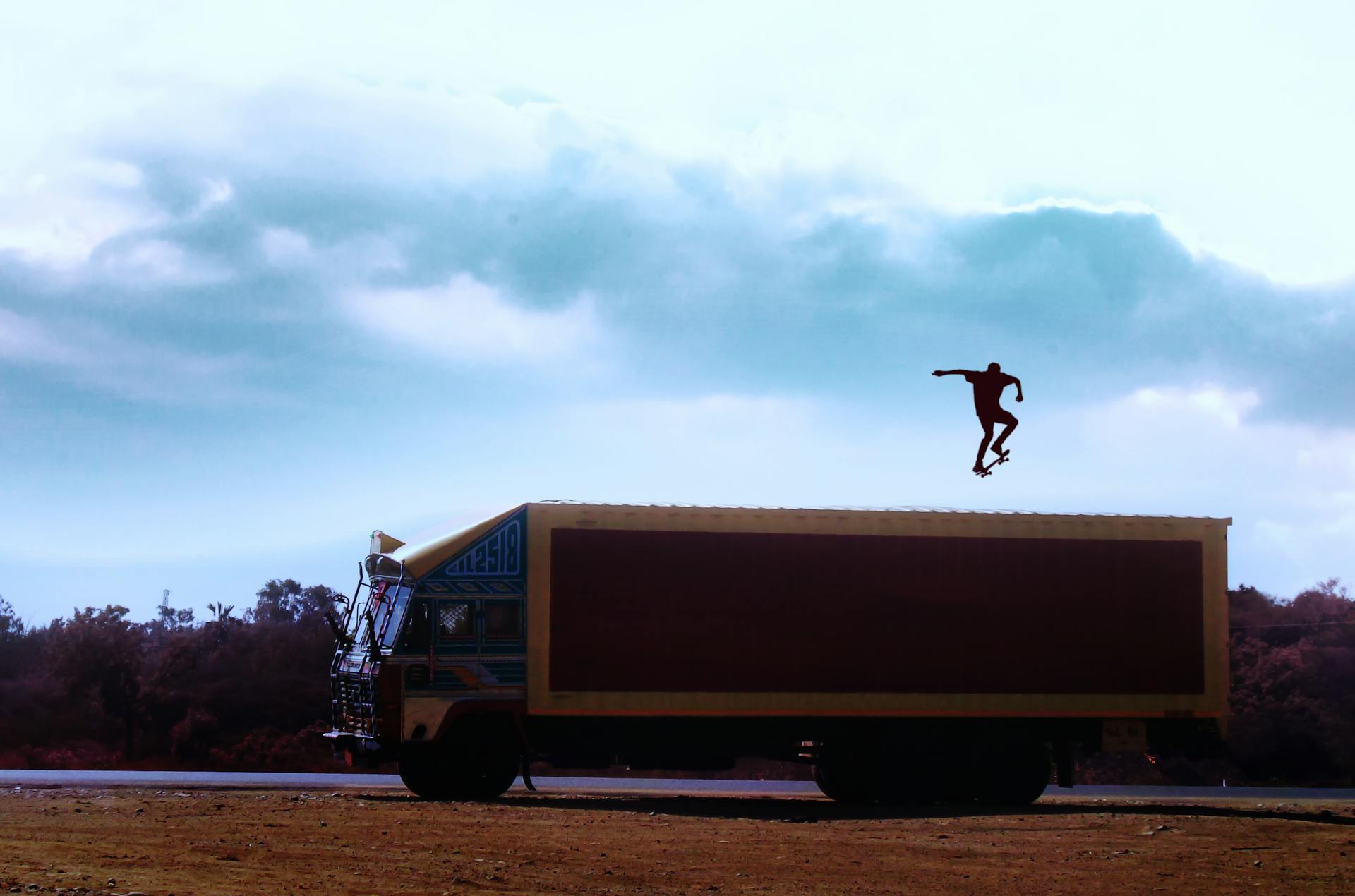 Dramatic shot of skateboarder mid-air atop a truck against a cloudy sky.
