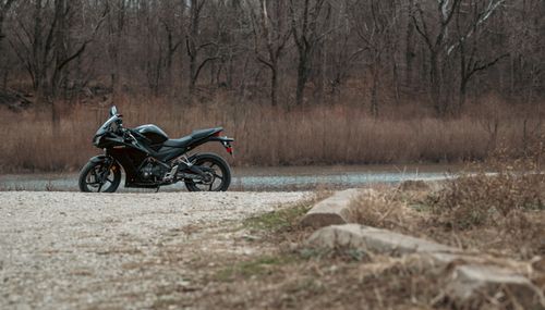 Free A black motorcycle parked on a gravel path in a serene forest landscape, near a calm lake. Stock Photo