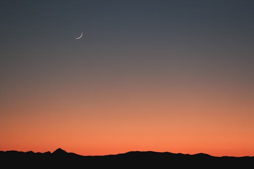 Moon Crescent over a Hilly Landscape at Dusk
