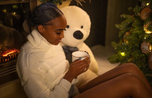 Happy Woman in Knitwear with Warm Drink near Christmas Tree