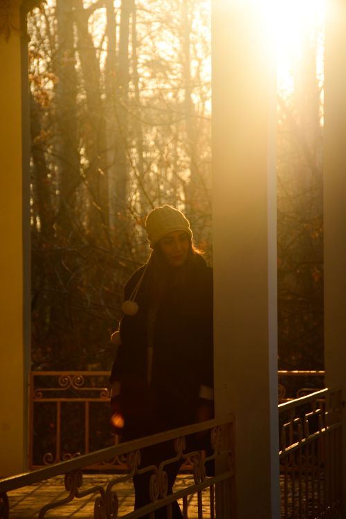 Free Backlit portrait of a woman wearing a beanie and jacket in a park with sunlit background. Stock Photo