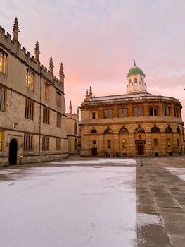 Snowy scene of the Sheldonian Theatre in Oxford with a winter sunset backdrop.