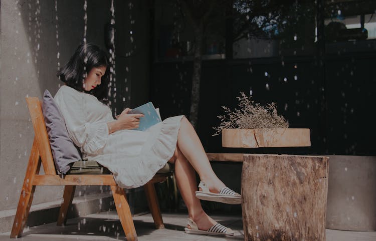 Photography Of A Sitting On Chair While Reading Book