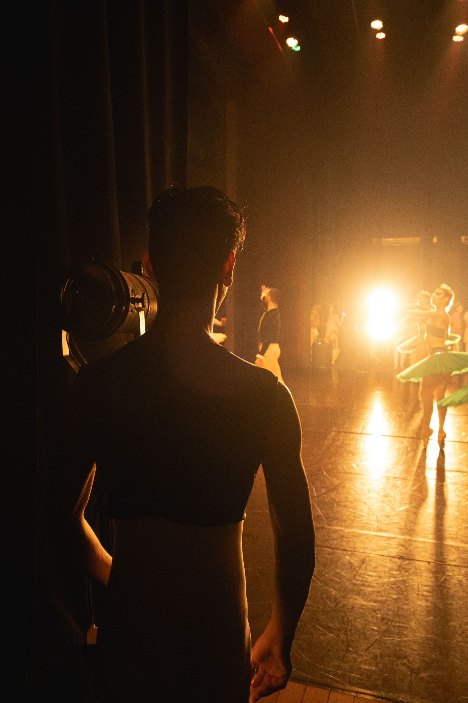 Bailarín entre bastidores mirando hacia el escenario iluminado