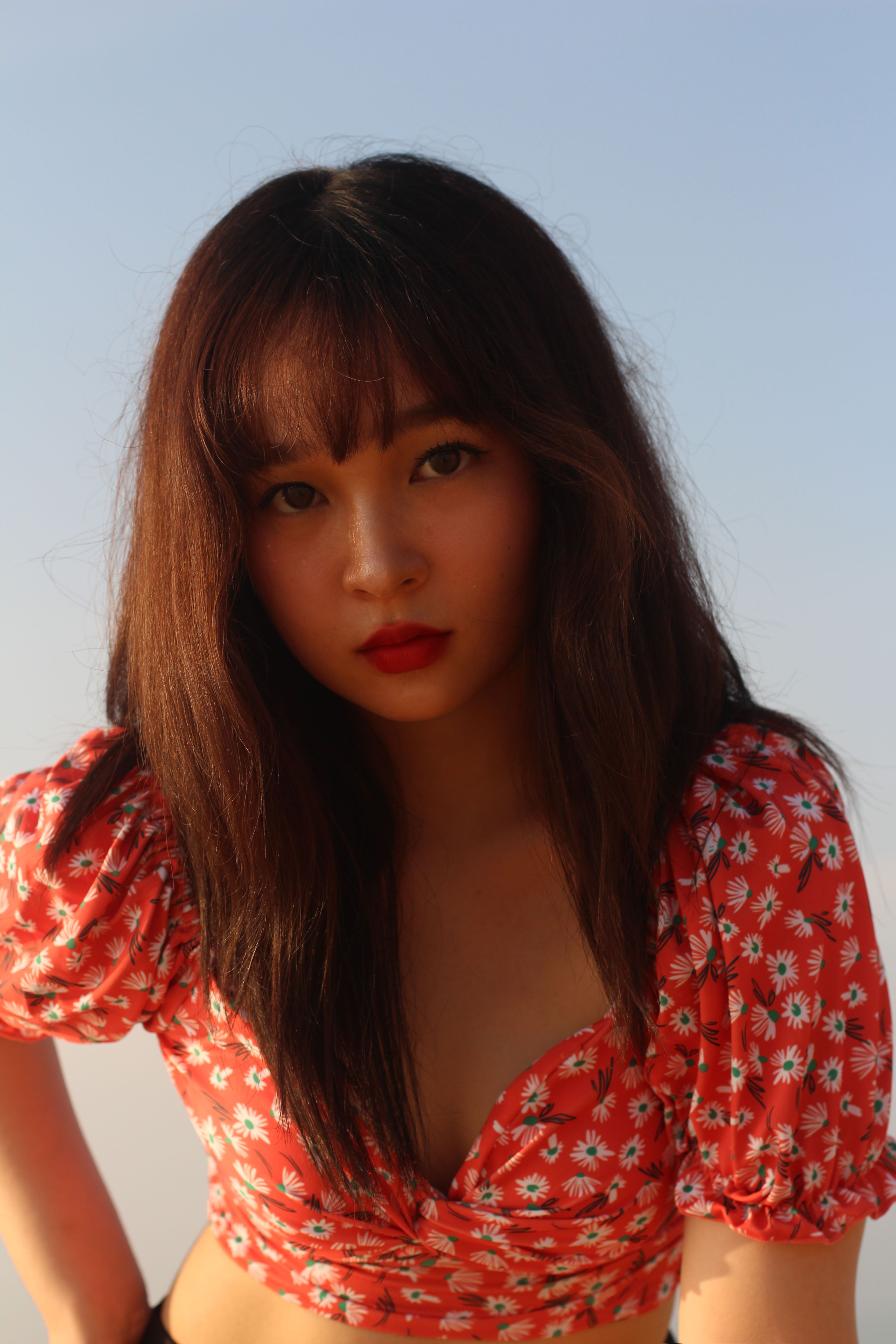 Portrait of a young woman wearing a floral crop top and red lipstick outdoors.
