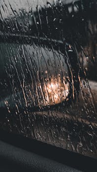 Close-up of raindrops on a car window with blurred lights at night, creating a moody atmosphere.