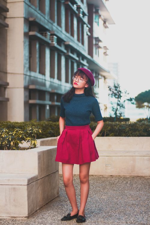 Free Chic Asian woman in red skirt and beret posing confidently in outdoor urban setting. Stock Photo
