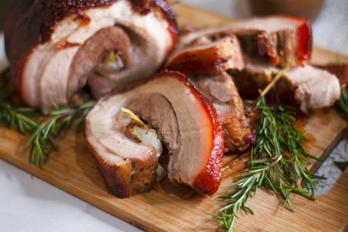 Free Delicious roasted porchetta slices on a wooden board with rosemary garnish, showcasing Italian cuisine. Stock Photo