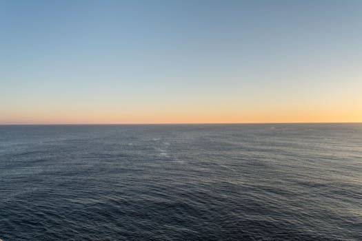 Peaceful open ocean at sunset with a clear horizon and gentle color transitions in the sky.