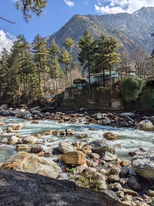 Free Serene mountain stream flowing through rocky landscape surrounded by lush forest and high peaks. Stock Photo