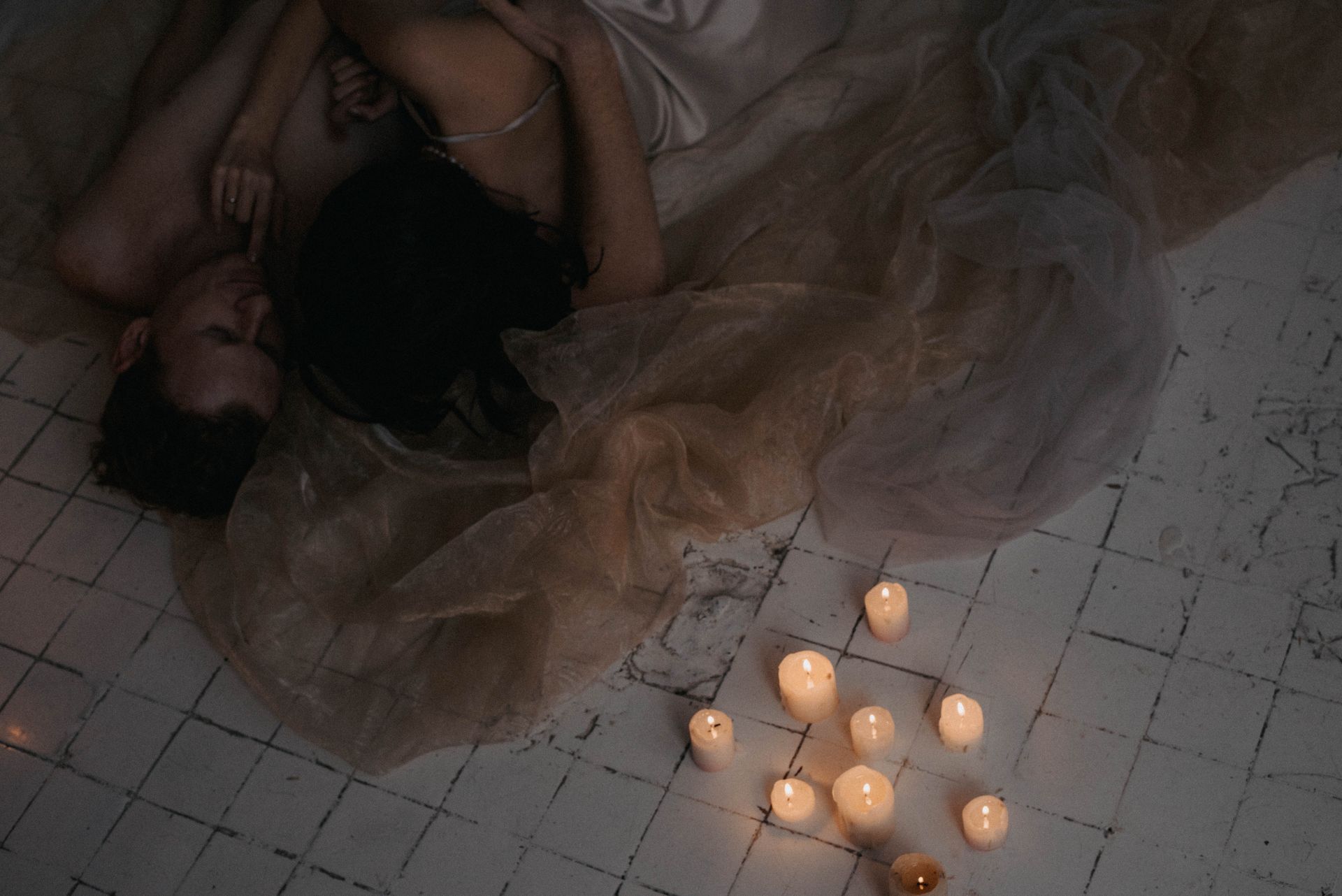 A couple embraces romantically on a rustic floor surrounded by candles, creating a warm atmosphere.