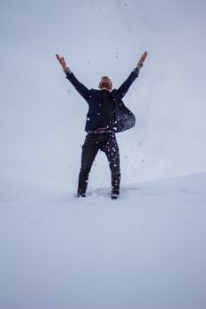 A man joyfully throwing snow into the air in a winter landscape, expressing freedom and happiness.