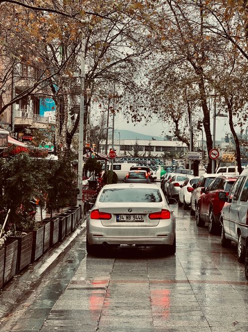 Free Wet city street with parked cars and flowing traffic in an urban setting, overcast weather conditions. Stock Photo