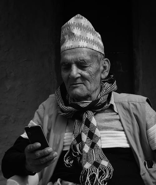 Grayscale Photo of an Elderly Man Using a Smartphone