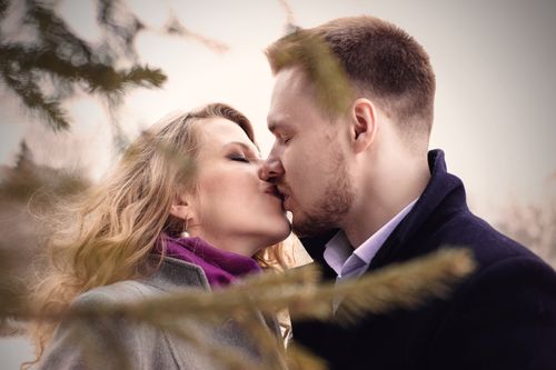 Free A couple sharing a kiss outdoors, surrounded by winter trees, capturing a moment of love and affection. Stock Photo