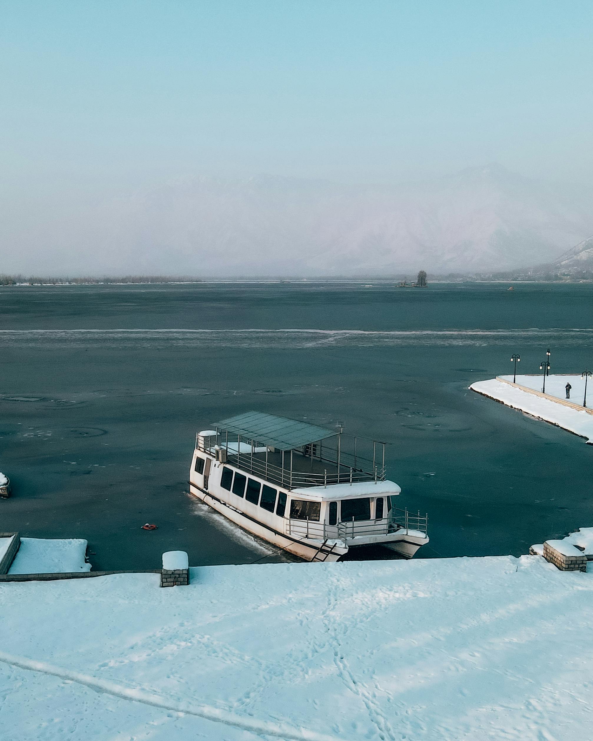 A picturesque winter view of a boat docked on the frozen Dal Lake in Srinagar, surrounded by snow.