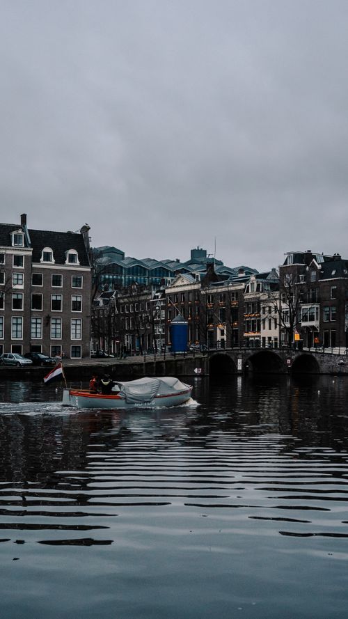 Free A peaceful motorboat glides through an Amsterdam canal, showcasing historic architecture. Stock Photo