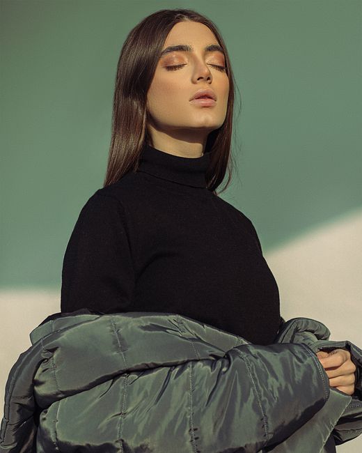A woman in a winter coat enjoys sunlight with eyes closed, capturing calmness and relaxation.