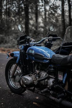 Close-up of a blue vintage motorcycle parked on a forest road with a blurred background.