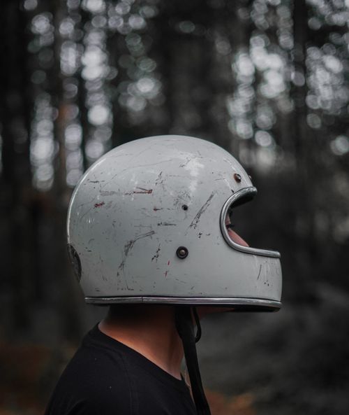 Free A close-up of a scratched motorcycle helmet worn by a person in a forest setting. Stock Photo