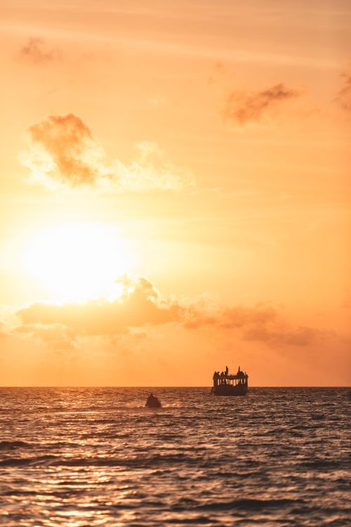 Free Silhouette of a boat against a vibrant sunset over a calm ocean. Stock Photo