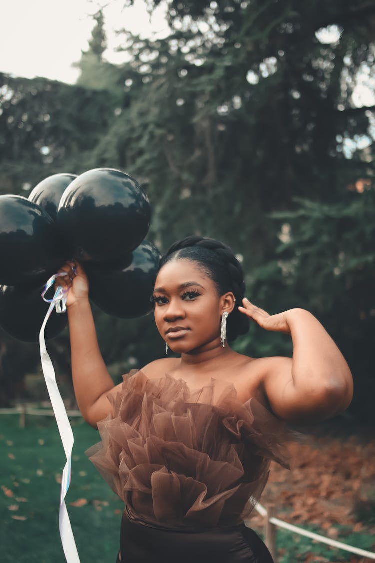 A Woman In Brown Dress Holding Latex Balloons