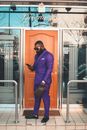 Man in Violet Suit Standing in Front of Wooden Door while Using His Cellphone