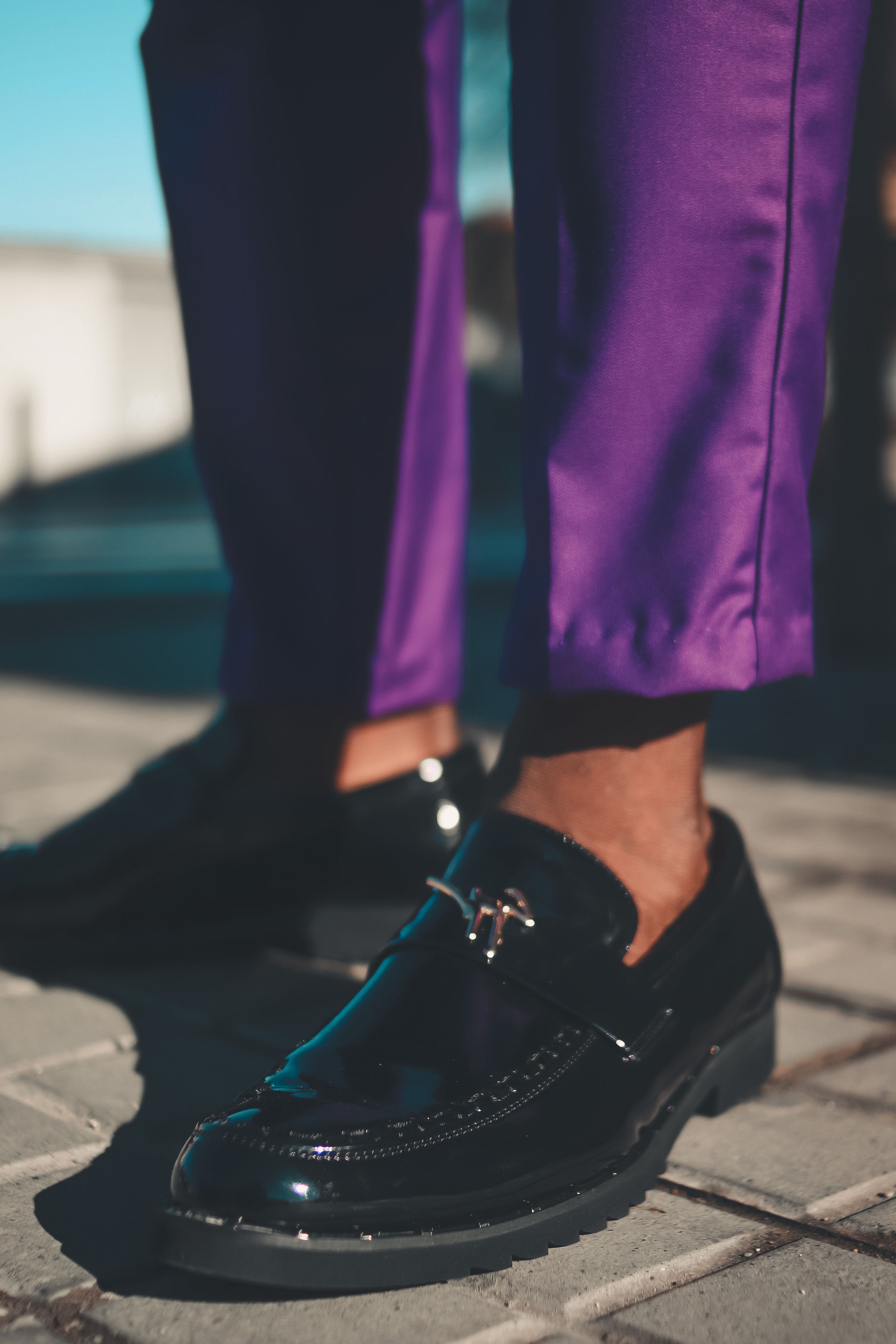 Mocassins pretos elegantes combinados com calças roxas em pavimento de pedra. Estilo urbano em luz natural.