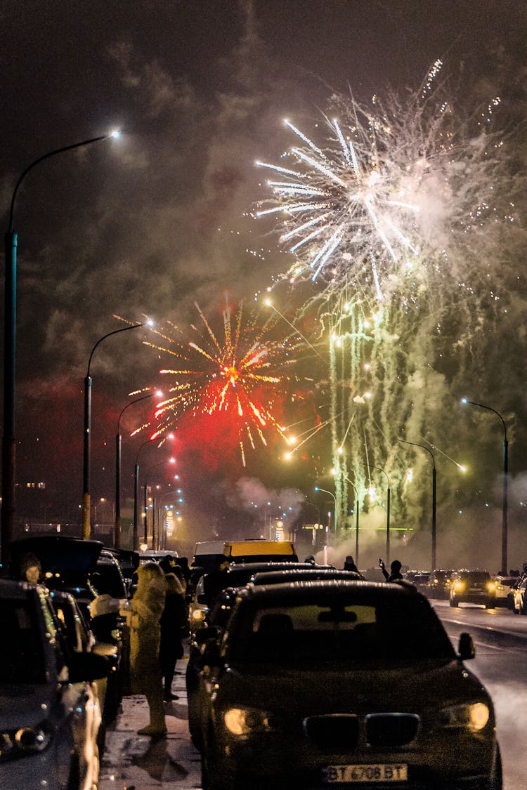 Cars Parked On The Street With Fireworks In The Sky At Night