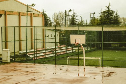 Free Empty outdoor basketball court with wet surface, surrounded by trees and buildings, captured during daytime. Stock Photo