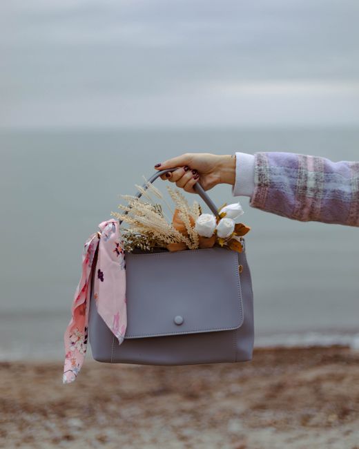 Stylish handbag held by a woman contains a beautiful bouquet, set against a serene beach backdrop.