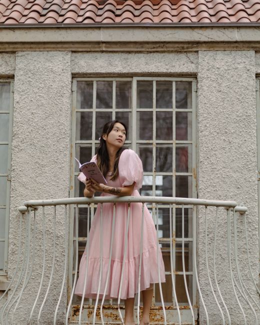 A woman in a pink dress reads a book on a balcony, conveying elegance and leisure.