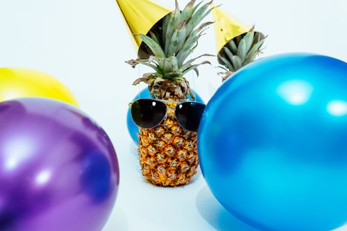 Free A fun party scene with a pineapple wearing sunglasses, surrounded by colorful balloons and hats. Stock Photo
