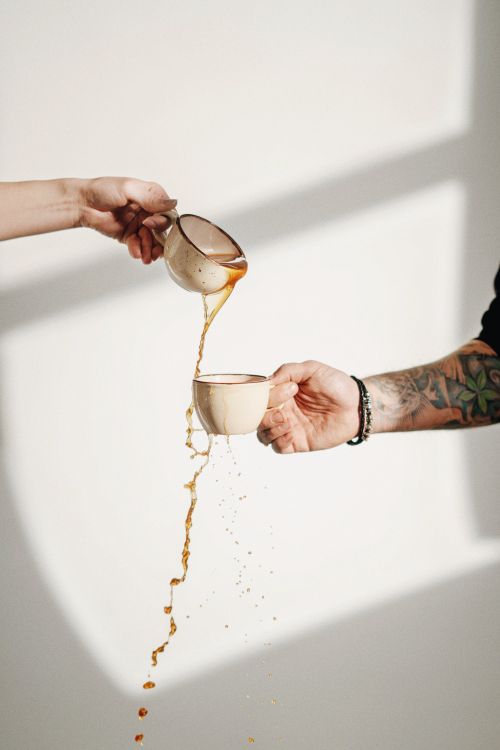 Free Dynamic coffee pour between hands, casting shadows with tattoo detail. Stock Photo