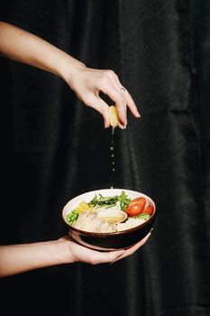 Hand squeezing lemon over a fresh salad bowl with vegetables. Perfect for food photography.