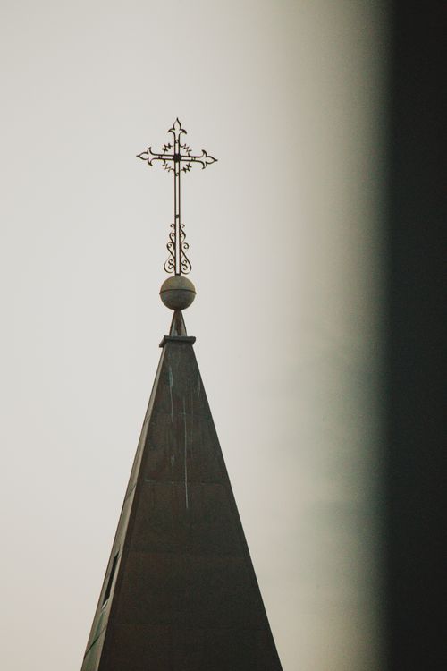 Free Close-up of a church steeple with an ornate cross against a sunset sky, symbolizing spirituality and faith. Stock Photo