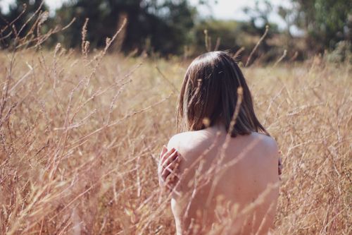 Free Nude woman sitting in a dry grass field, embracing nature. Stock Photo