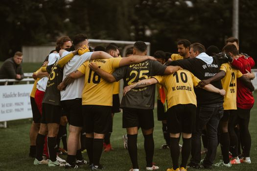 A soccer team in yellow and black jerseys huddles together on a grassy field, showing unity and teamwork.