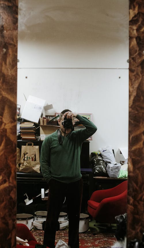 Man in Green Sweater Taking Photo in Front of a Mirror