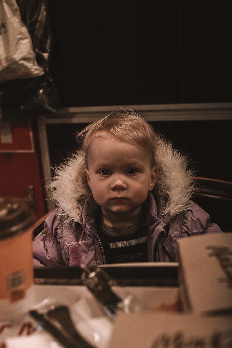 Boy With Serious Facial Expression Sitting In An Interior, Wearing A Winter Jacket