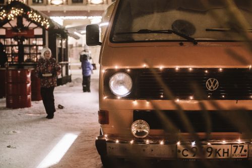 Free A vintage van decorated with lights parked on a snowy street during a winter night market. Stock Photo