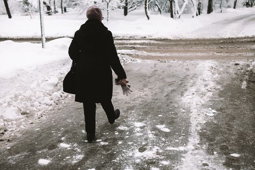 A person in a trench coat walks on a snowy road, embracing the winter weather.