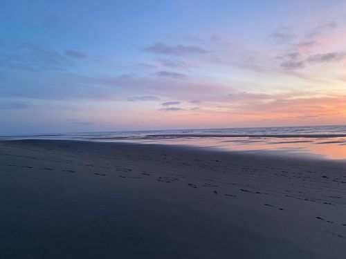 Free Stunning sunset at the beach with wet sand reflecting pastel colors and footprints. Stock Photo