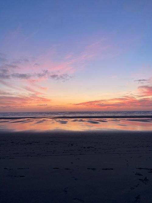 Free A peaceful sunset over a calm ocean with a dramatic sky and sandy beach foreground. Stock Photo