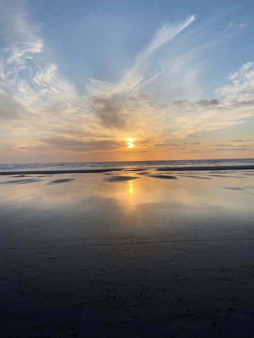 Free Peaceful sunrise over the ocean with reflective water and sandy beach. Stock Photo