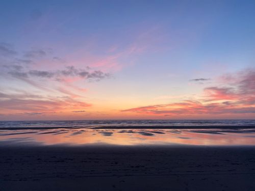 Free Stunning sunset view over a serene ocean with dramatic skies reflecting on wet sand. Stock Photo