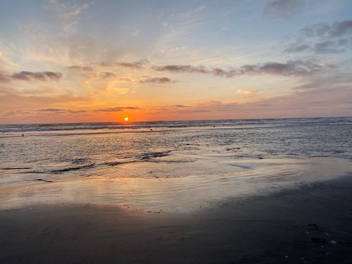 Free Beautiful sunset over a tranquil beach with calm waves and clouds in the sky. Stock Photo