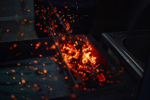 Vibrant sparks fly from glowing coal in a dark furnace, creating a dynamic fiery scene.