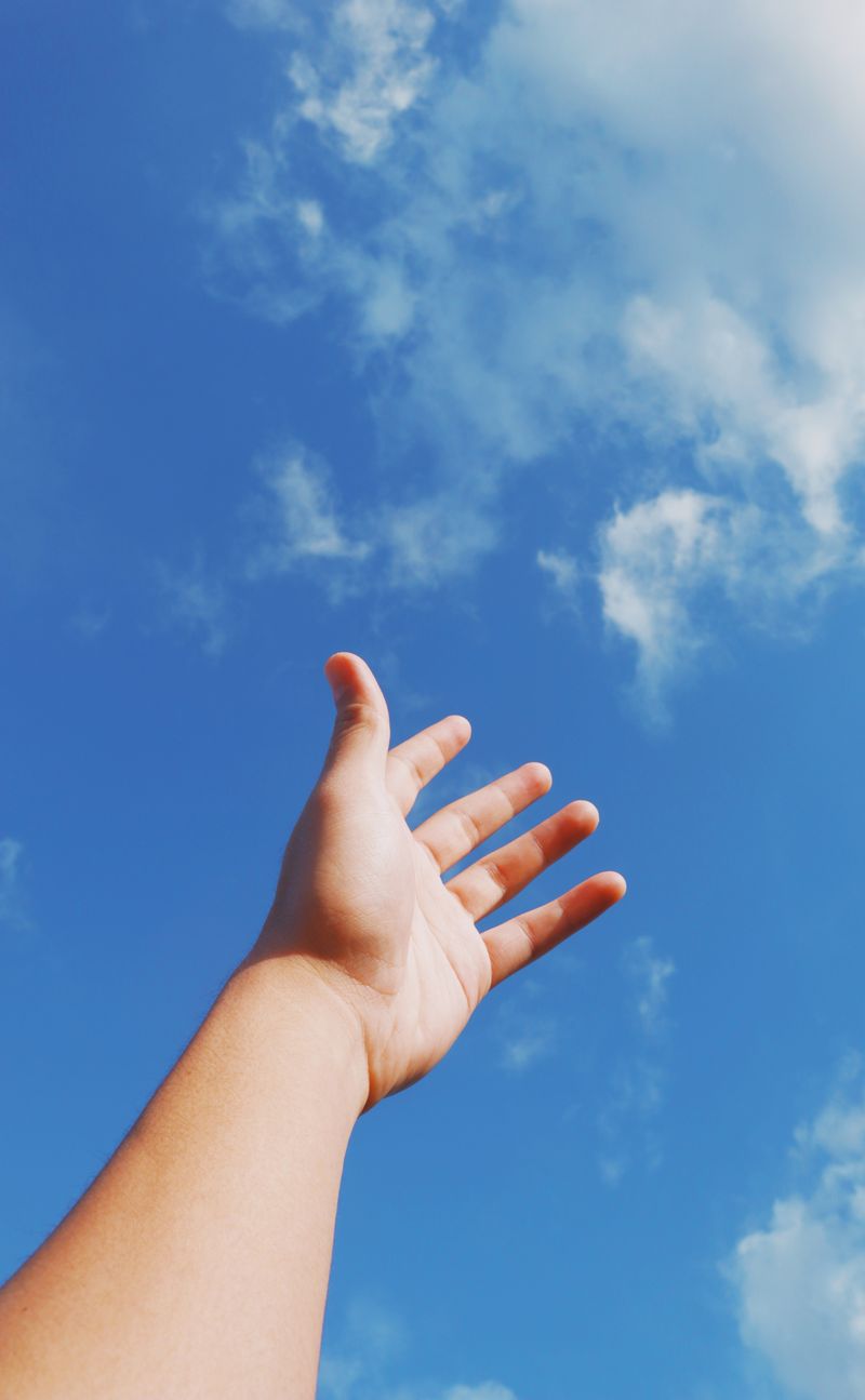 A hand reaching up into an open sky. Photo by Nothing Ahead on Pexels
