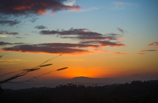 A stunning sunset over distant hills, capturing the dramatic colors of the sky with silhouettes of surrounding nature.